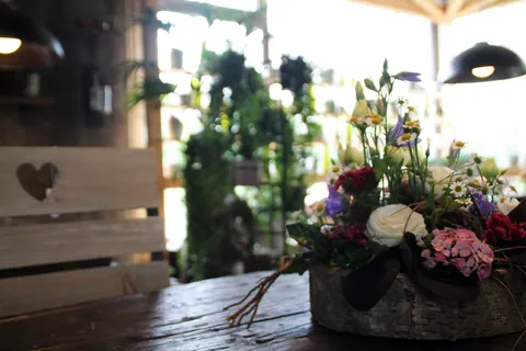 Blumengesteck mit Rosen und Hortensien neben einem Holzherz